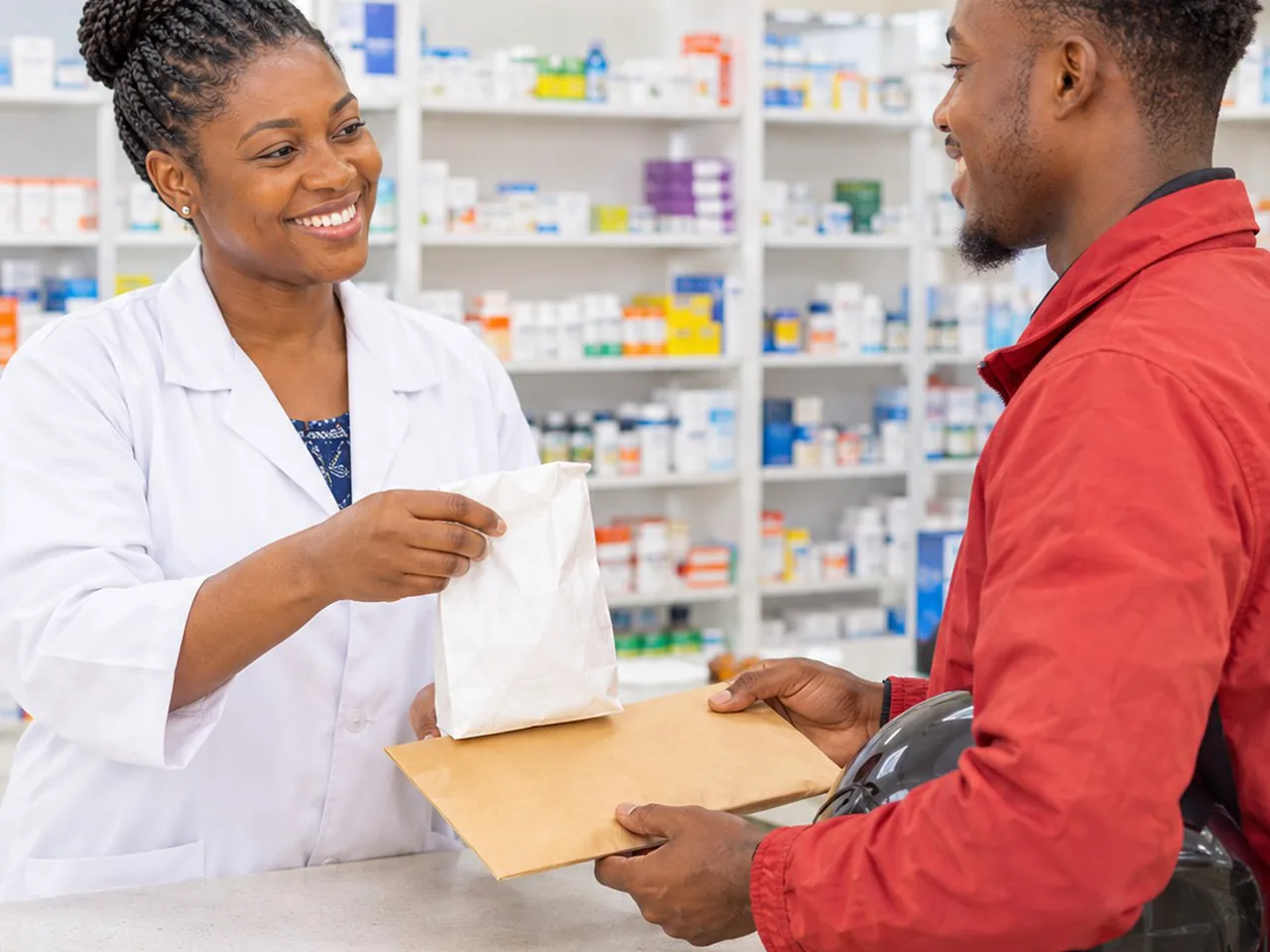 A pharmacist handing a sealed pharmacy bag and an envelope to a Seaton Swift rider